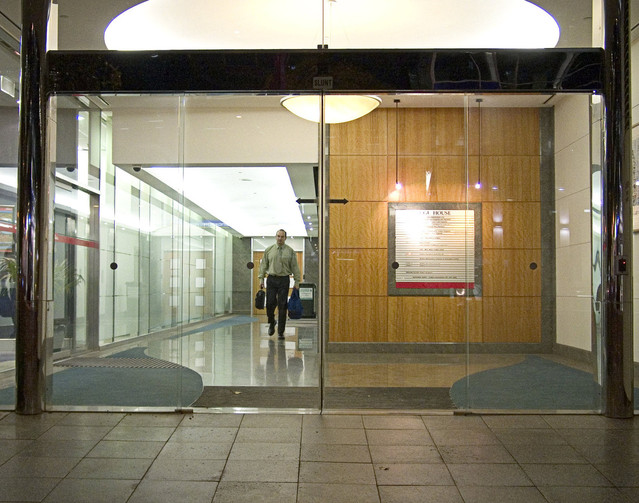 Kancelária, muž kráča s kufrom v ruke, sklenené steny, sklenené dvere