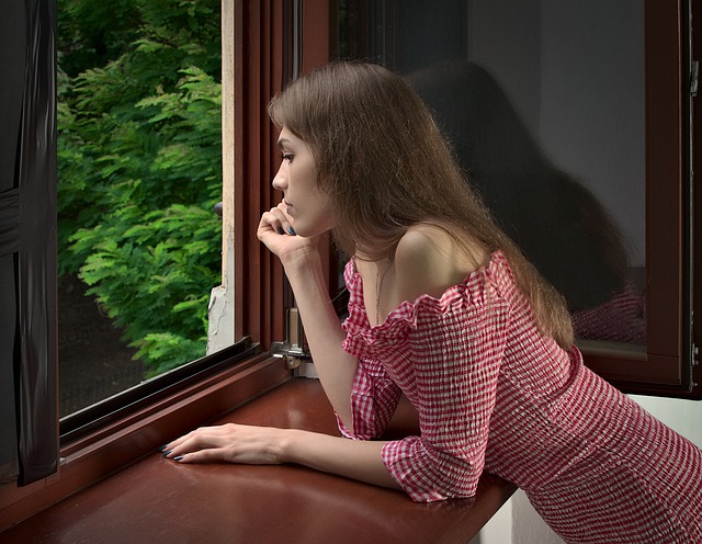 Žena sa pozerá von z okna s drevenými rámami na stromy.jpg