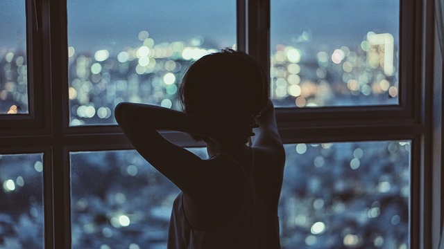 Žena stojí pri veľkom okne a pozerá na nočné mesto.jpg